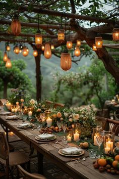 an outdoor dinner table with candles and greenery on the table, surrounded by hanging lanterns