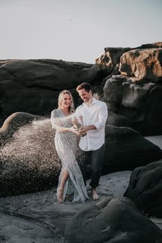 a man and woman are standing on the beach with sand blowing in front of them