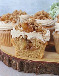 several cupcakes with white frosting and toppings on a wooden platter