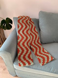 an orange and white knitted scarf sitting on top of a blue couch next to a potted plant