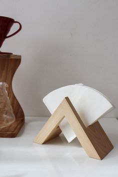 a wooden object sitting on top of a white counter next to a vase and cup