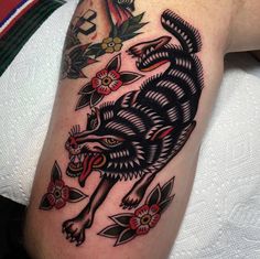 a black and grey wolf tattoo on the right arm with red flowers around its neck