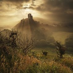 the sun shines through the clouds over a castle on top of a hill with trees