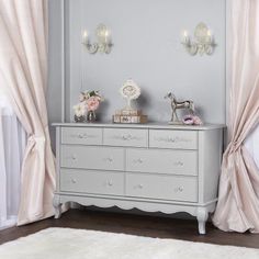 a white dresser sitting next to a window covered in pink curtained drapes and flowers