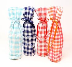 three wine bottles wrapped in plaid fabric and tied with orange ribbon, one blue, the other red