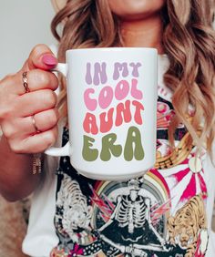 a woman holding a white coffee mug with the words in my cool aunt era on it