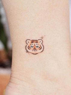 a small tiger tattoo on the side of a woman's ankle, with an orange and black tiger face