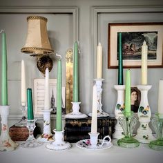 a table topped with lots of different types of candles next to pictures on the wall