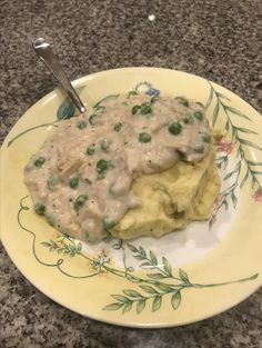 a yellow plate topped with mashed potatoes covered in gravy next to a fork