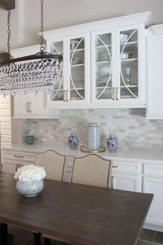 a chandelier hanging from the ceiling above a wooden table in a white kitchen