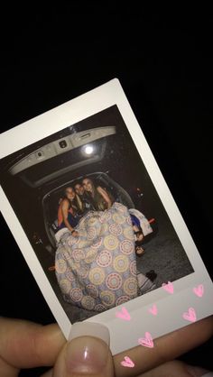 a person holding up a polaroid with the image of three people in a car