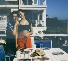 two people standing next to each other in front of a table with food on it