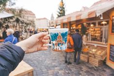 a person holding up a coffee cup in front of a building with people walking around