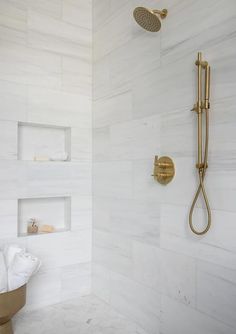 a white bathroom with gold fixtures and marble tiles on the shower wall, along with toilet paper