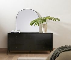 a black dresser with mirror and plant on it in a room that has hardwood floors