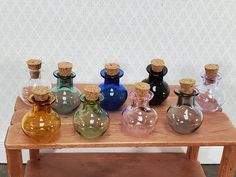 several different colored glass bottles sitting on a wooden table in front of a white wall