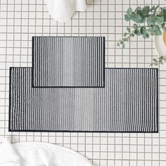 two black and white bathroom rugs sitting on top of a tiled floor next to a potted plant