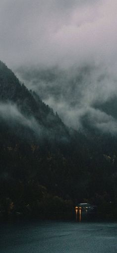 the mountains are covered in fog and low lying clouds as they sit on the water