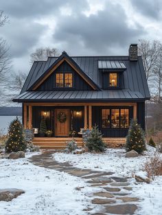 a house with a black metal roof and christmas trees in the front yard on a snowy day