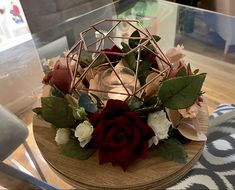 a wooden table topped with a vase filled with red and white flowers next to a candle