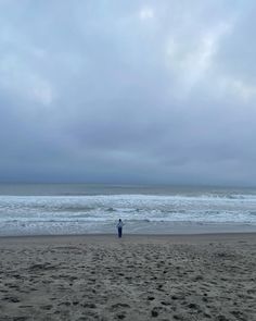 a man standing on top of a beach next to the ocean under a cloudy sky