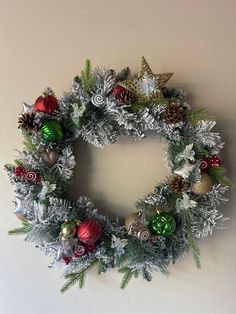 a christmas wreath hanging on the wall next to a white wall with silver and red ornaments