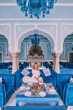 a woman sitting on top of a blue couch in front of a chandelier