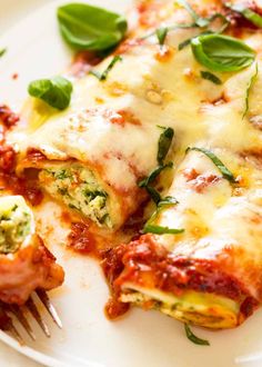 a white plate topped with lasagna covered in cheese and spinach garnish