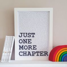 a white shelf topped with books next to a rainbow bookend and a framed poster