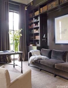 a living room filled with furniture and bookshelves next to a window covered in curtains