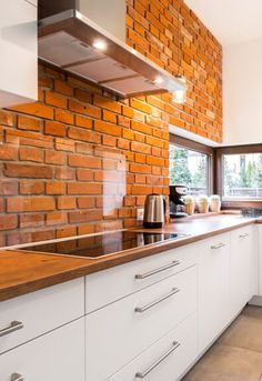 a brick wall in a kitchen with white cabinets and counter tops, along with an oven