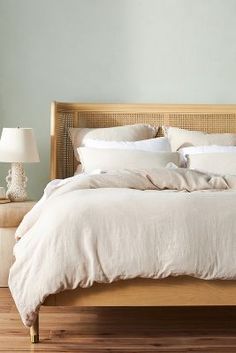 a bed with white linens and pillows in a light colored room next to a night stand