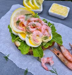 an open face sandwich with shrimp, lettuce and boiled eggs on it next to lemon wedges