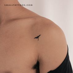 a small tattoo on the back of a woman's left shoulder, with a bird flying above it