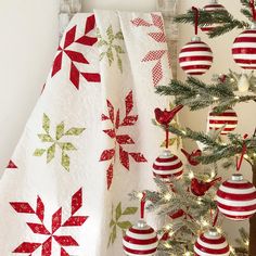 a christmas tree with red and green ornaments on it next to a quilted wall hanging