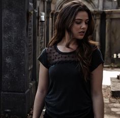 a woman in black shirt walking down street next to stone wall and building with arched doorway