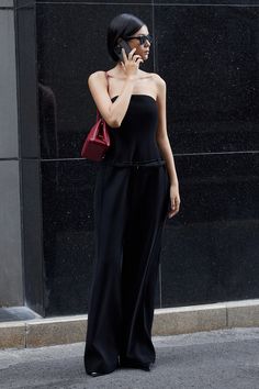 a woman in black is talking on her cell phone while walking down the street with a red handbag