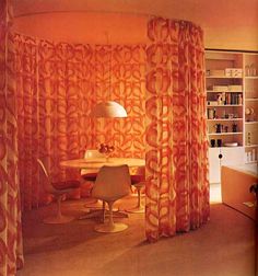 an orange curtained room with a table and chairs in it, next to a book shelf