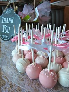 cake pops are arranged on a clear plate with pink and white candies in the middle