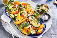 a white plate topped with a salad covered in veggies and dressing next to two spoons