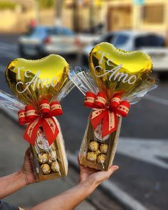 two heart shaped chocolates wrapped in foil and tied with red ribbon are held by someone's hand