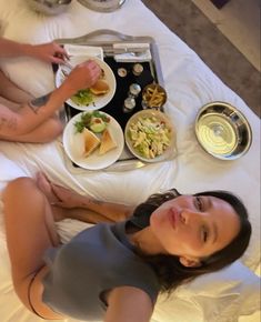 two women sitting on a bed with plates of food