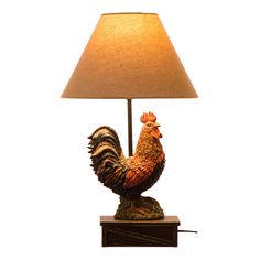 a rooster lamp sitting on top of a wooden table next to a brown shade lampshade