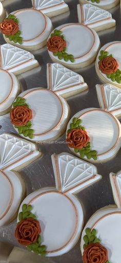 decorated cookies are arranged in rows on a baking sheet, with orange roses and green leaves