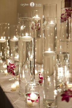 candles are lit on the table with flowers and petals in glass vases next to each other