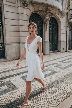 a woman is walking down the street wearing a white dress and sandals with her hand on her hip