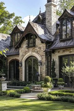 a large stone house with lots of windows and plants in the front yard, surrounded by greenery