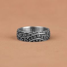 a silver ring with flowers and leaves on the inside, sitting on a brown surface