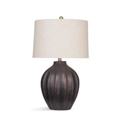 a table lamp with a white shade on it and a brown vase underneath the lamp