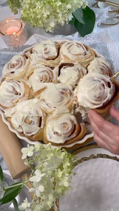 a person is decorating a cake with icing on it and flowers in the background